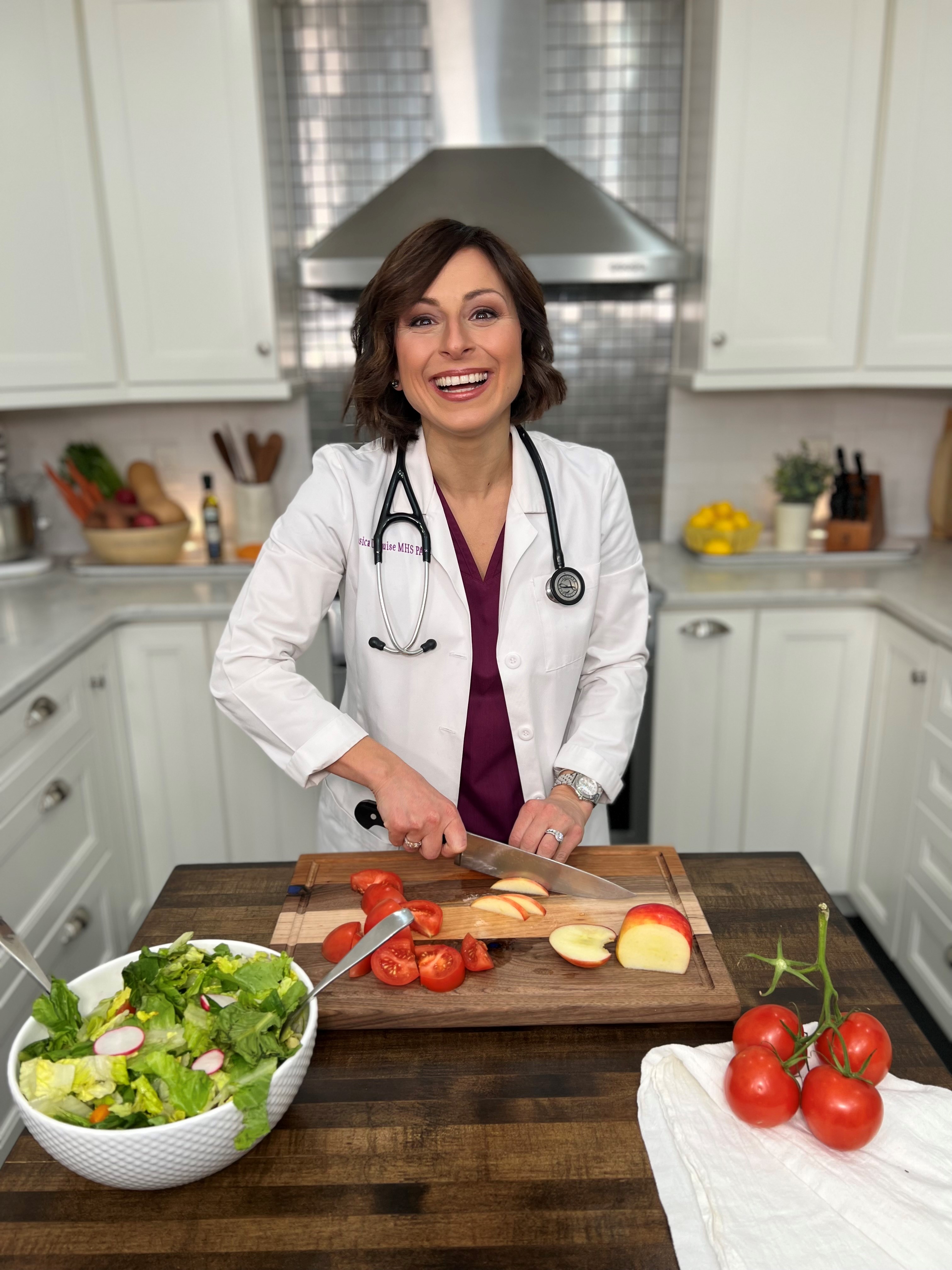 Alumna Jessica DeLuise wearing white coat and stethoscope in kitchen preparing healthy food